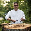 Zu sehen ist Rostislav Balciunas vor einem abgesägten Baum mit Drumsticks in der Hand.