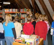 Eine Mitarbeiterin der Stadtbibliothek erläutert während einer Führung die Ordnung der Kinder- und Jugendbücher ab 12 Jahren.