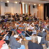 Zu sehen sind die Jugendlichen mit Instrumenten in einer Orchesterformation bei einer Probe in einem Musiksaal
