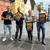 Zu sehen sind die Verantwortlichen der Veranstaltung mit einem Plakat in der Hand auf dem unteren Markplatz stehend