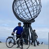 Zu sehen ist ein Mann mit einem Fahrrad an dem Aussichtspunkt des Nordkaps mit einer Globusstatue